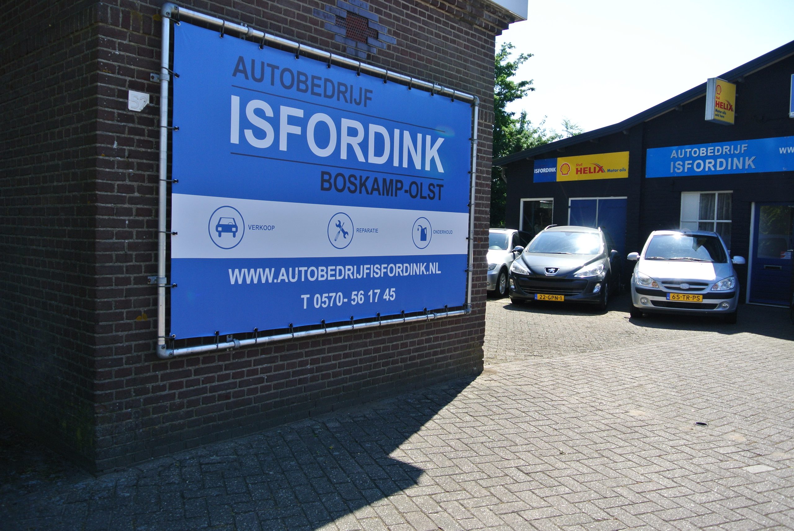 Het spandoek van Autobedrijf Isfordink Boskamp-Olst op de bakstenen muur, rechts het pand